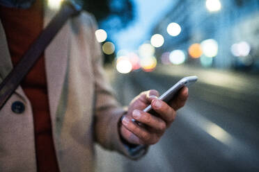 A midsection view of businessman with smartphone standing on a street in the evening. A close-up. - HPIF30449