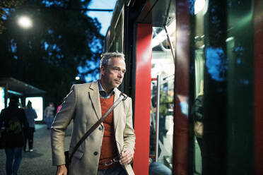 Reifer Geschäftsmann mit Koffer, der abends in Prag in eine Straßenbahn oder einen Oberleitungswagen einsteigt. - HPIF30451