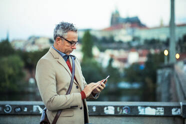 Älterer Geschäftsmann mit Smartphone steht auf einer Brücke in der Stadt, Textnachrichten. - HPIF30455