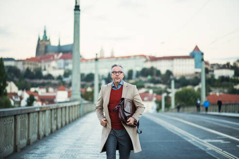 Reifer, gut aussehender Geschäftsmann mit Tasche, der auf einer Brücke in Prag spazieren geht, Kopierraum. - HPIF30459