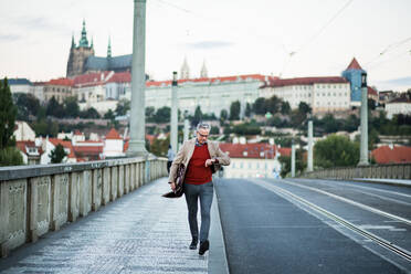 Reifer, gutaussehender Geschäftsmann mit Tasche, der auf einer Brücke in Prag spazieren geht und die Zeit prüft. Kopierraum. - HPIF30460
