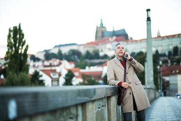 Mature businessman with smartphone standing on a bridge in city, making a phone call. - HPIF30463