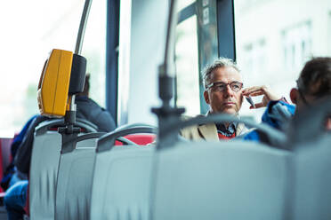 Mature handsome businessman with smartphone travellling by bus in city, making phone call. Copy space. - HPIF30476