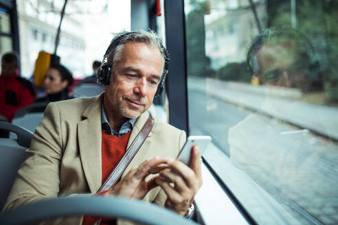 Reifer, müder Geschäftsmann mit Smartphone und Heaphones, der mit dem Bus in der Stadt unterwegs ist und Musik hört. - HPIF30479