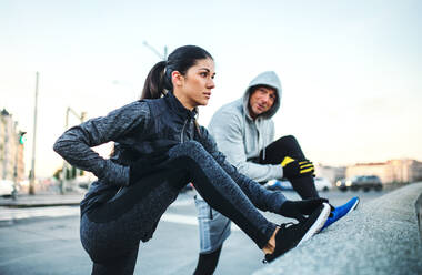 A fit sporty couple runners doing stretching outdoors on the bridge in Prague city, Czech Republic. - HPIF30488