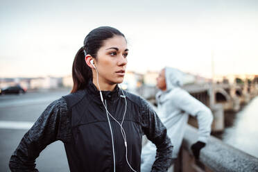 Eine fitte junge Läuferin mit Kopfhörern steht im Freien auf einer Brücke in Prag und hört Musik. - HPIF30490