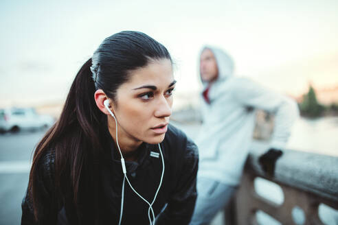 Eine fitte junge Läuferin mit Kopfhörern steht im Freien auf einer Brücke in Prag und hört Musik. - HPIF30491
