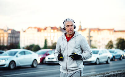 Ein fitter reifer männlicher Läufer mit Kopfhörern läuft im Freien auf der Brücke in Prag und hört Musik. - HPIF30497