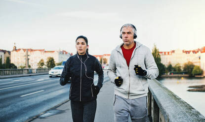 Ein sportliches Paar mit Kopfhörern, das im Freien auf einer Brücke in Prag läuft und Musik hört. - HPIF30505