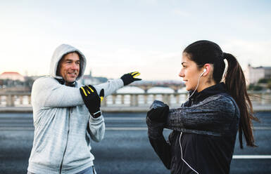 A fit sporty couple runners doing stretching outdoors on the bridge in Prague city, Czech Republic. - HPIF30510