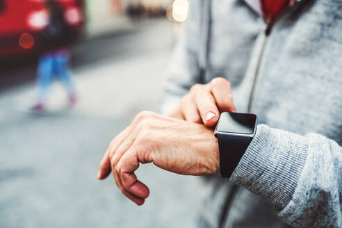 Nahaufnahme der Hände eines nicht erkennbaren Mannes, der draußen in der Stadt steht und eine Smartwatch benutzt. - HPIF30519