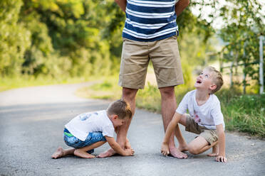 Zwei kleine Söhne spielen mit einem nicht erkennbaren Vater an einem Sommertag auf einer Straße im Park und zeichnen mit Kreide. - HPIF30544