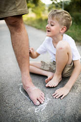 Ein kleiner Junge spielt mit seinem Vater an einem Sommertag auf einer Straße im Park und zeichnet mit Kreide. - HPIF30547