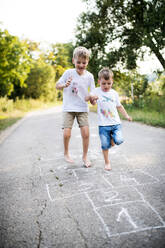 Zwei barfuß laufende, fröhliche kleine Jungen, die an einem Sommertag auf einer Straße im Park herumhüpfen. - HPIF30550