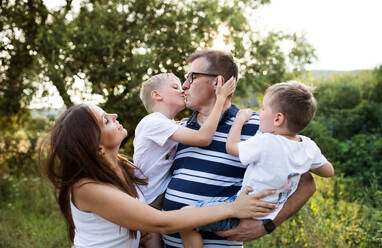 A cheerful young family holding two small sons outdoors in nature on a summer day, standing. - HPIF30552