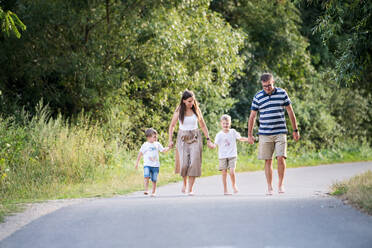 A young family with two small cheerful sons walking barefoot on a road in park on a summer day, holding hands. - HPIF30557