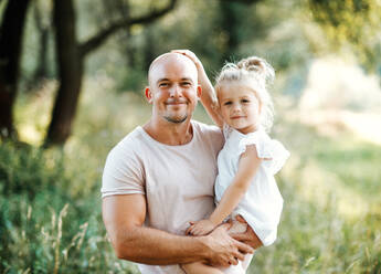 Gut aussehender junger Vater in grüner, sonniger Sommernatur, der seine süße kleine Tochter in den Armen hält. - HPIF30560
