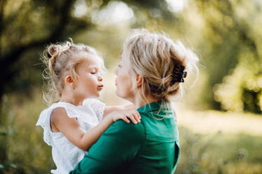 Beautiful young mother in green sunny summer nature holding her cute small daughter in the arms. - HPIF30564