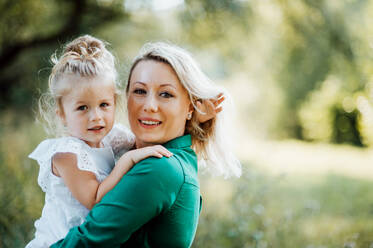 Beautiful young mother in green sunny summer nature holding her cute small daughter in the arms. Copy space. - HPIF30565