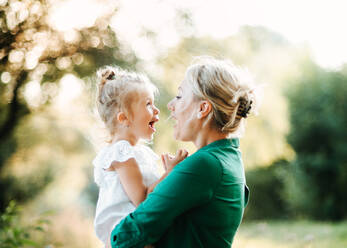 Schöne junge Mutter in grüner sonniger Sommernatur hält ihre süße kleine Tochter in den Armen. - HPIF30575