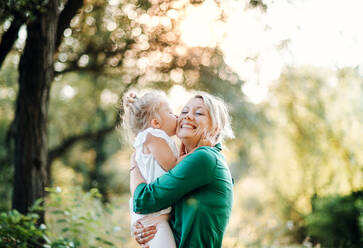 Junge Mutter mit kleiner Tochter auf einer Wiese in der Natur, küssend. - HPIF30576