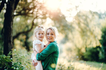 Schöne junge Mutter in grüner sonniger Sommernatur hält ihre süße kleine Tochter in den Armen. - HPIF30577