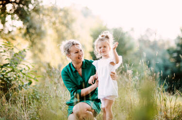 Schöne junge Mutter in grüner sonniger Sommernatur hält ihre süße kleine Tochter. - HPIF30579
