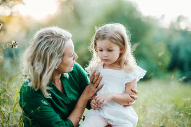 Schöne junge Mutter in grüner sonniger Sommernatur hält ihre süße kleine Tochter. - HPIF30587