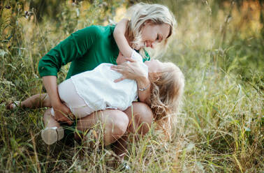 Schöne junge Mutter in grüner sonniger Sommernatur hält ihre süße kleine Tochter. - HPIF30589