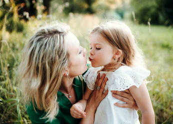 Junge Mutter mit kleiner Tochter auf einer Wiese in der Natur, küssend. - HPIF30590