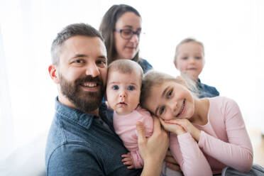 Ein Porträt einer glücklichen jungen Familie mit kleinen Kindern, die drinnen auf einem Sofa sitzen. - HPIF30595