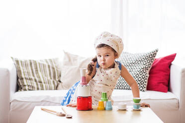 Ein süßes kleines Mädchen mit Schürze und Hut spielt zu Hause. - HPIF30613