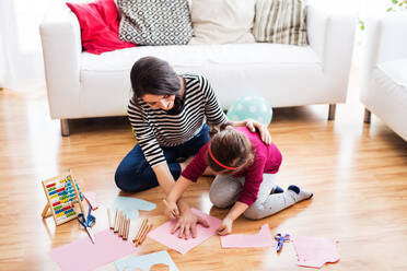 Junge Mutter mit einem kleinen Mädchen zu Hause, die auf dem Boden sitzt und zeichnet. - HPIF30616