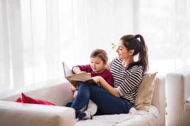 Junge schöne Mutter mit einem kleinen Mädchen zu Hause, die ein Buch liest. - HPIF30622