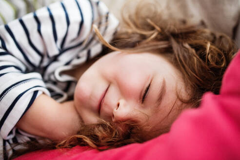 Ein süßes, kleines, glückliches Mädchen im gestreiften T-Shirt, das zu Hause schläft, Nahaufnahme. - HPIF30629