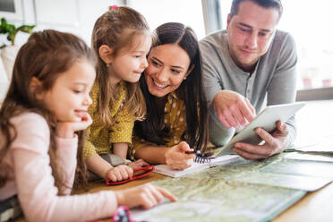 Junge glückliche Familie mit zwei Kindern und Tablet, die sich auf den Urlaub zu Hause vorbereitet. - HPIF30656