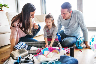 Porträt einer jungen, glücklichen Familie mit einem Kind beim Packen für den Urlaub zu Hause. - HPIF30666