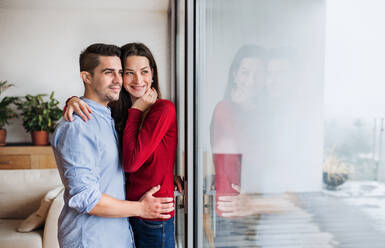 Junges, glückliches, verliebtes Paar, das zu Hause am Fenster steht und sich umarmt. Kopierraum. - HPIF30692