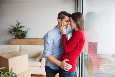 Ein junges, glückliches Paar zieht in ein neues Haus ein, steht am Fenster und umarmt sich. - HPIF30693