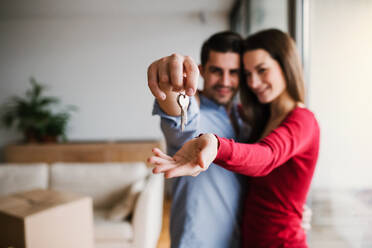 A young happy couple with a key and cardboard boxes standing indoors, moving in a new home. - HPIF30695