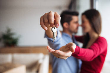 A young happy couple with a key and cardboard boxes standing indoors, moving in a new home. - HPIF30696