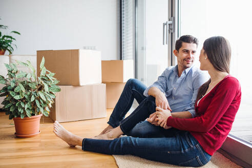 Ein junges, verliebtes Paar zieht in eine neue Wohnung ein, sitzt auf dem Boden und sieht sich an. - HPIF30697