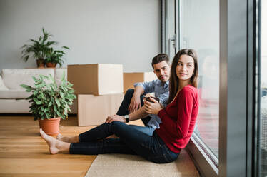 Ein junges, glückliches Paar, das mit Kartons in eine neue Wohnung umzieht, sitzt mit einem Kaffee auf dem Boden. - HPIF30698