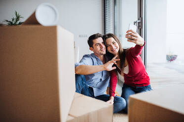 Ein junges Paar hält seine Aufregung über den Umzug in ein neues Haus in einem Selfie mit seinem Smartphone und Kartons fest - HPIF30705