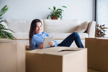 Eine junge Frau mit Tablet und Kartons, die auf dem Boden liegen, beim Umzug in eine neue Wohnung. - HPIF30714