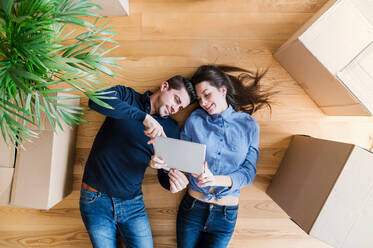Draufsicht auf ein junges Paar mit Tablet und Kartons, die auf dem Boden liegen, beim Umzug in eine neue Wohnung. - HPIF30716