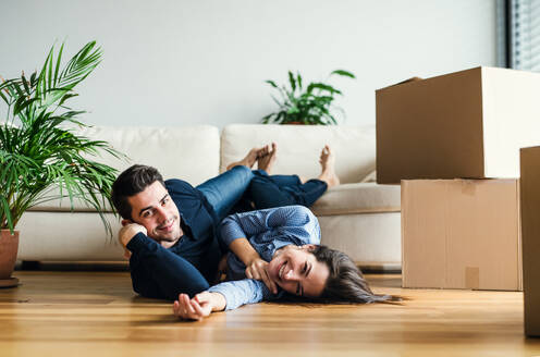 A young couple with cardboard boxes lying on the floor, moving in a new home. - HPIF30718