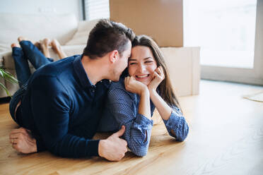 A young happy couple with a cup and cardboard boxes lying on a floor, moving in a new home. - HPIF30719