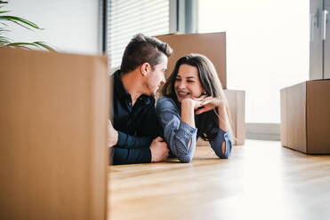 A young happy couple with a cup and cardboard boxes lying on a floor, moving in a new home. - HPIF30720