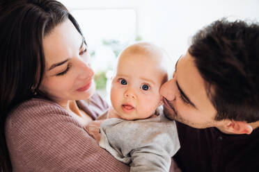 A close-up portrait of happy young couple with a baby indoors at home. - HPIF30736